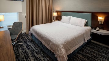 Une chambre d’hôtel avec un grand lit, un bureau avec une chaise, une lampe de bureau, un téléphone et un luminaire fixé au mur.