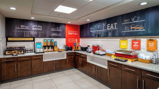 A modern kitchen with a breakfast bar, waffle station, and various food items displayed. - Hampton Inn Long Island / Commack (Commack)