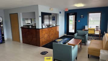 Un hall de hotel con mostrador de recepción, zona de estar y señal de suelo mojado.