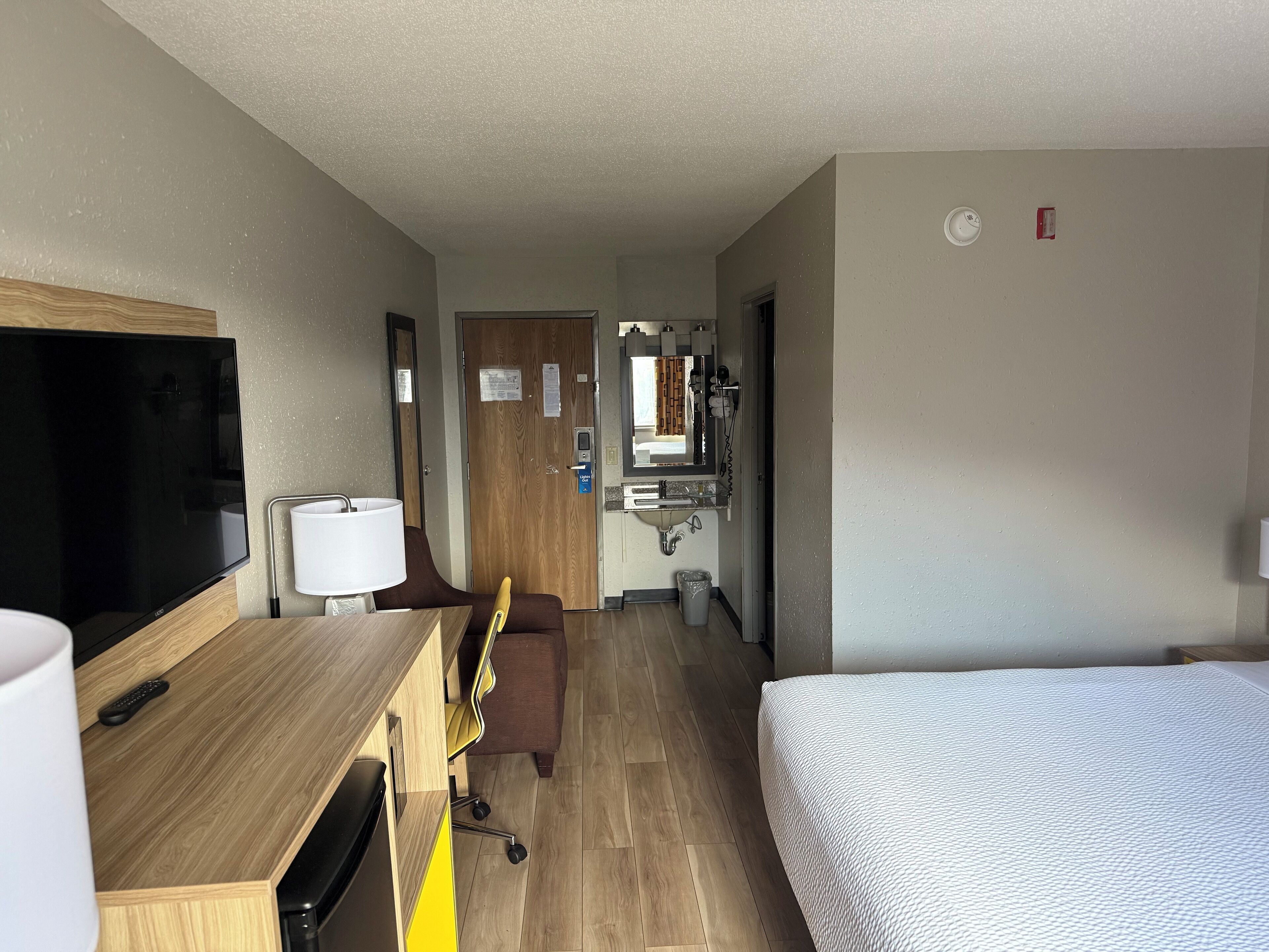 Hotelkamer met een bed, bureau met televisie, stoel, spiegel en een badkamer door een open deur zichtbaar.