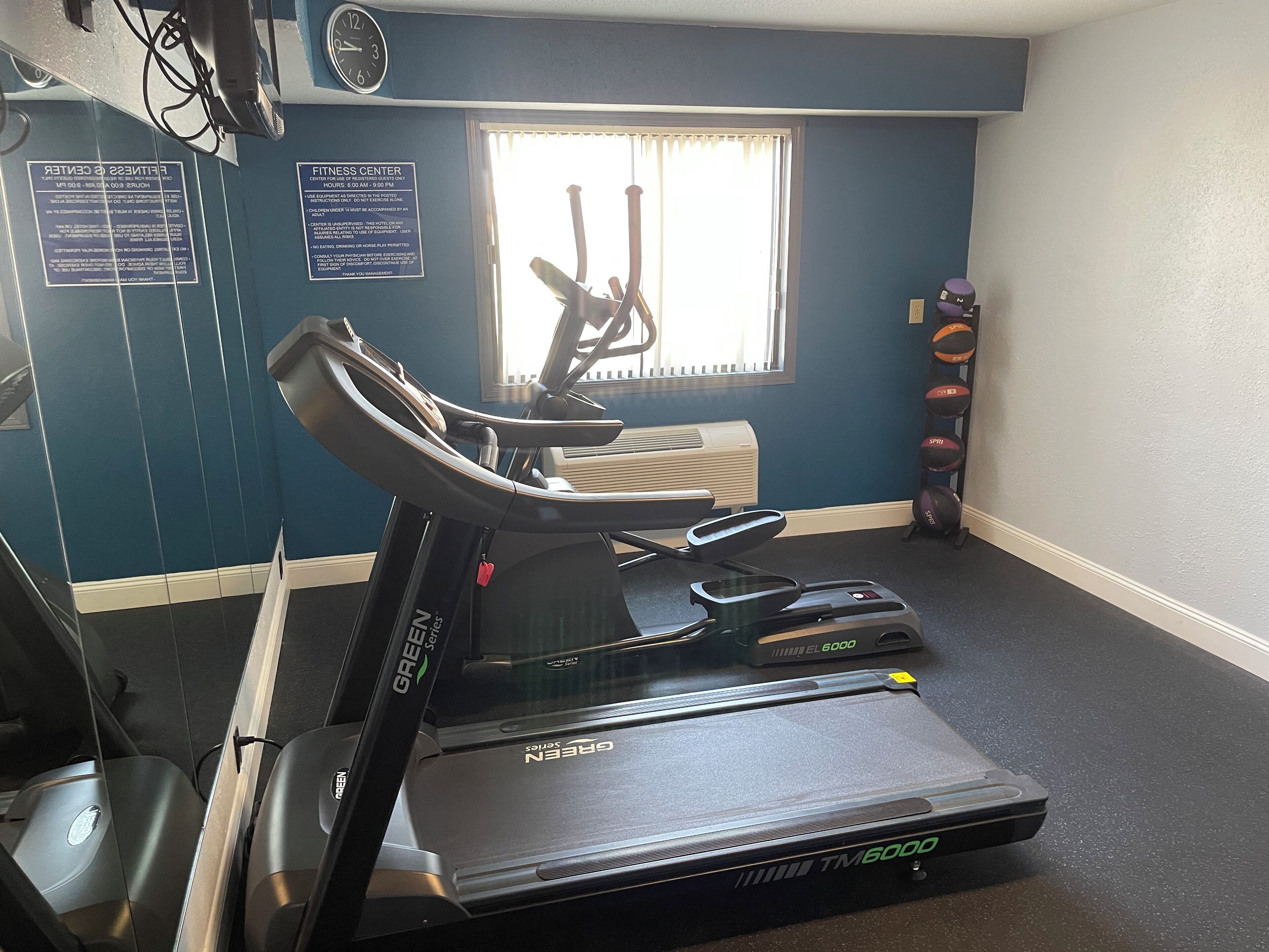 Ein Fitnessstudio mit Laufband, Ergometer und einem Fenster mit Jalousien.