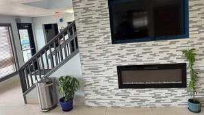 A modern hotel lobby with a staircase, a large wall-mounted TV, and two potted plants. - Days Inn by Wyndham Muncie -Ball State University (Muncie)