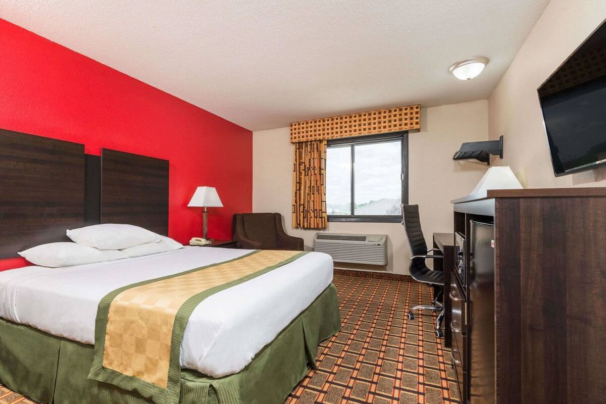 A hotel room with a bed, a desk, a chair, a TV, and a window with curtains.