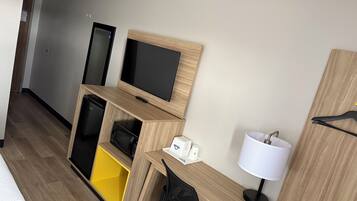 Una camera d'albergo con una scrivania in legno, una televisione, un forno a microonde, un piccolo mobiletto, una lampada e un letto.