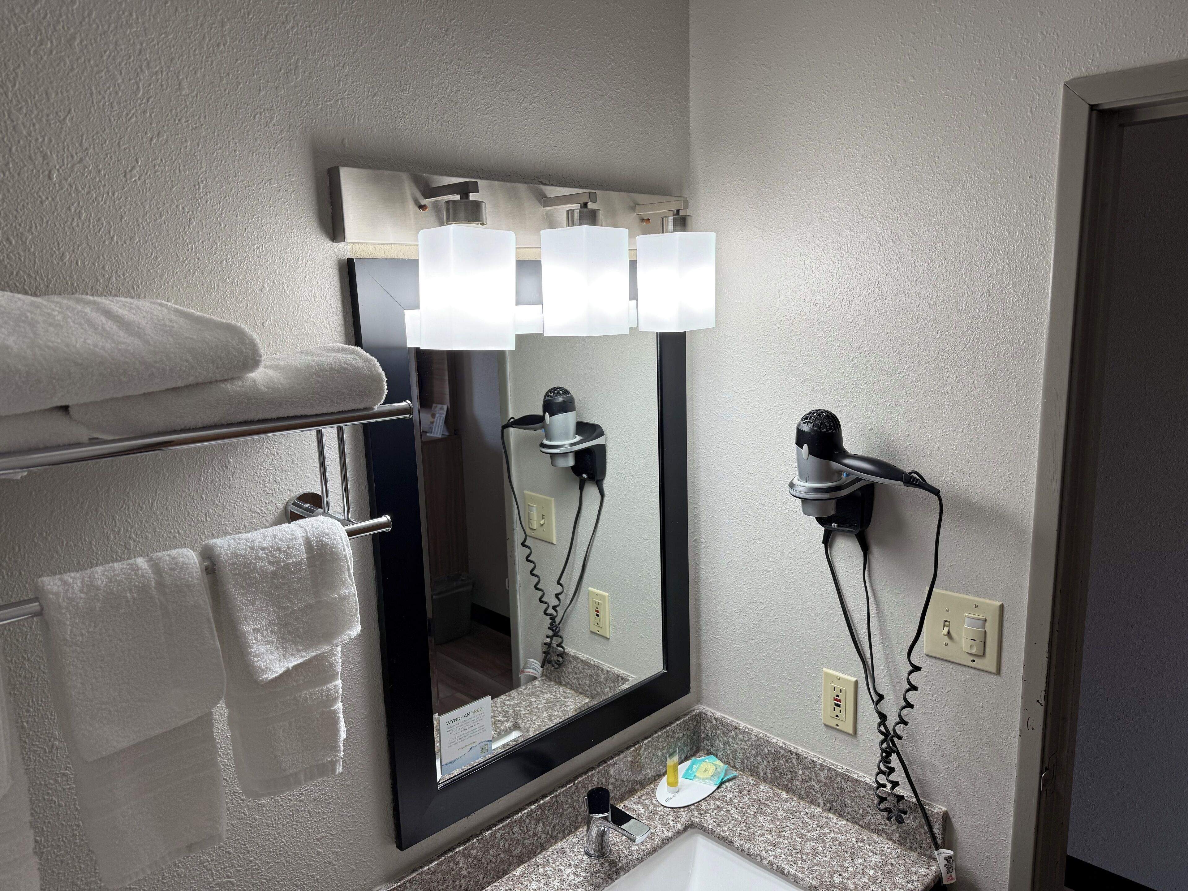 Un bagno con uno specchio grande, un porta asciugamani e un asciugacapelli su un supporto a parete.