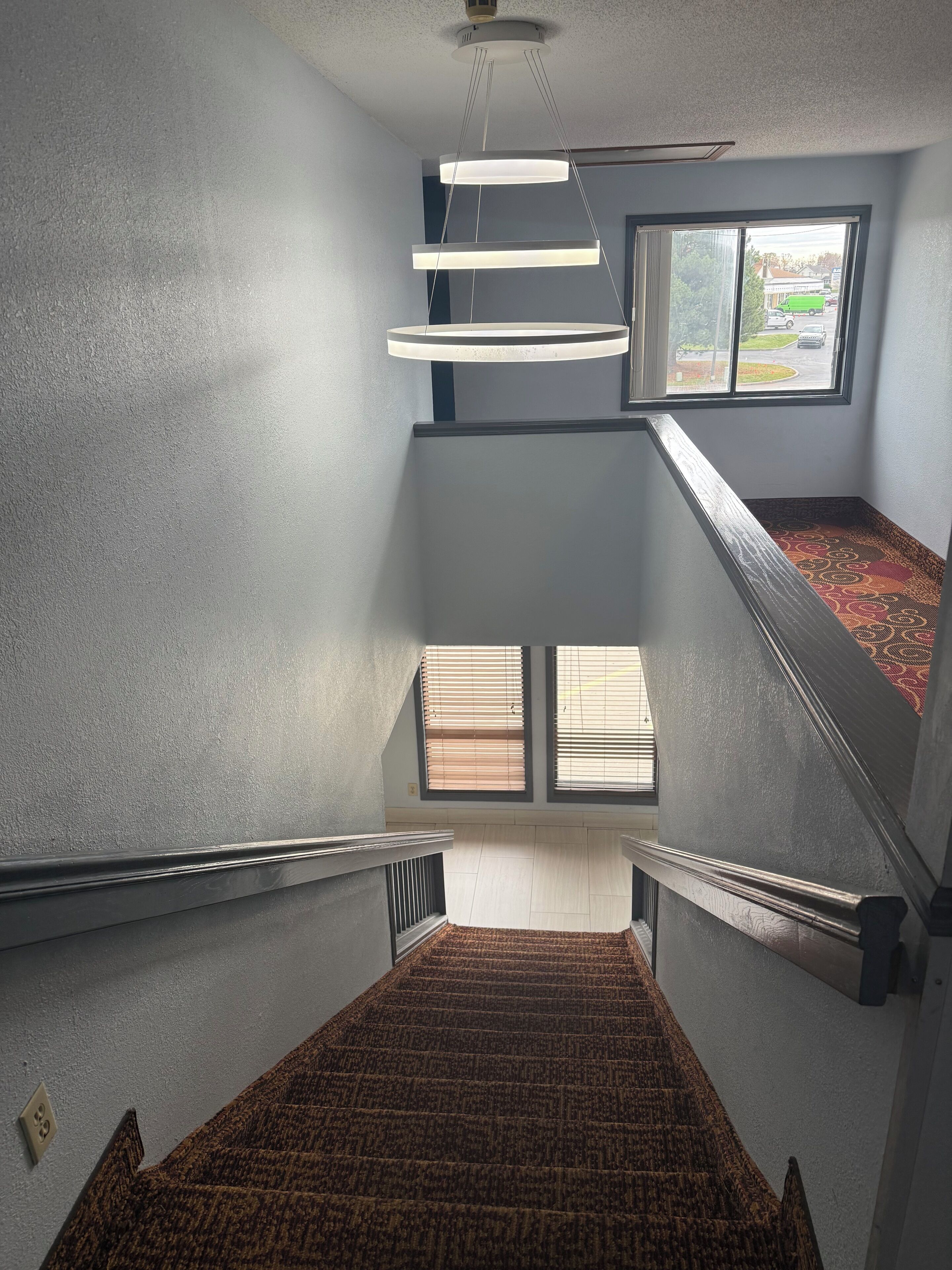 A staircase with a patterned carpet, a modern light fixture, and a window with blinds.