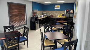 A restaurant with a blue and white color scheme, featuring a 'Daybreak Breakfast' sign, a kitchen area with a microwave and coffee machine, and several tables and chairs. - Days Inn by Wyndham Muncie -Ball State University (Muncie)