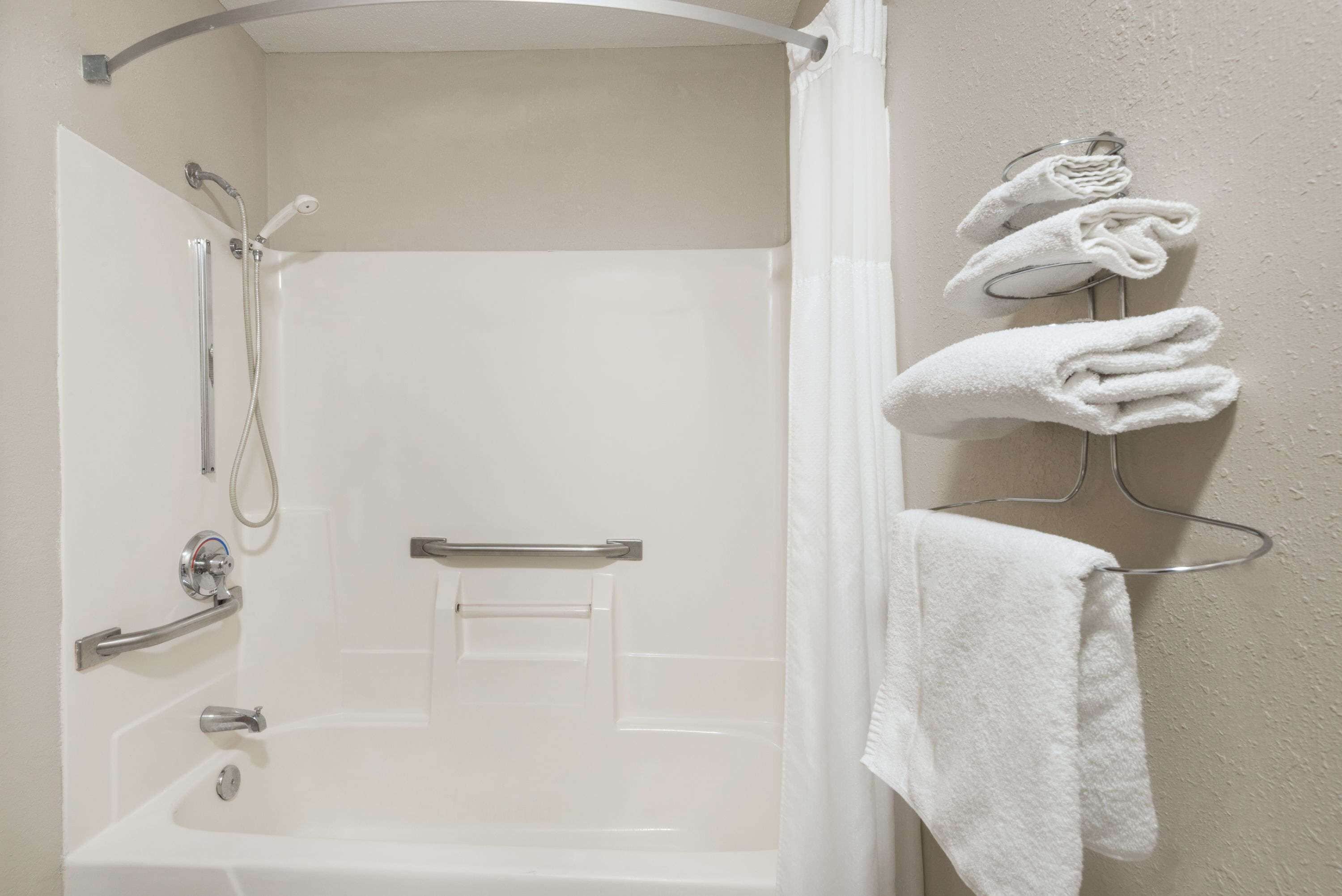 A bathroom with a shower, grab bars, a towel rack, and a towel hanging on the rack.