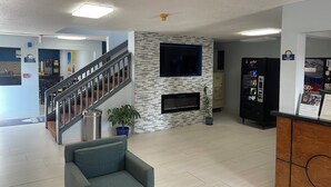 A modern lobby with a staircase, a seating area, a fireplace, vending machines, and a water dispenser. - Days Inn by Wyndham Muncie -Ball State University (Muncie)