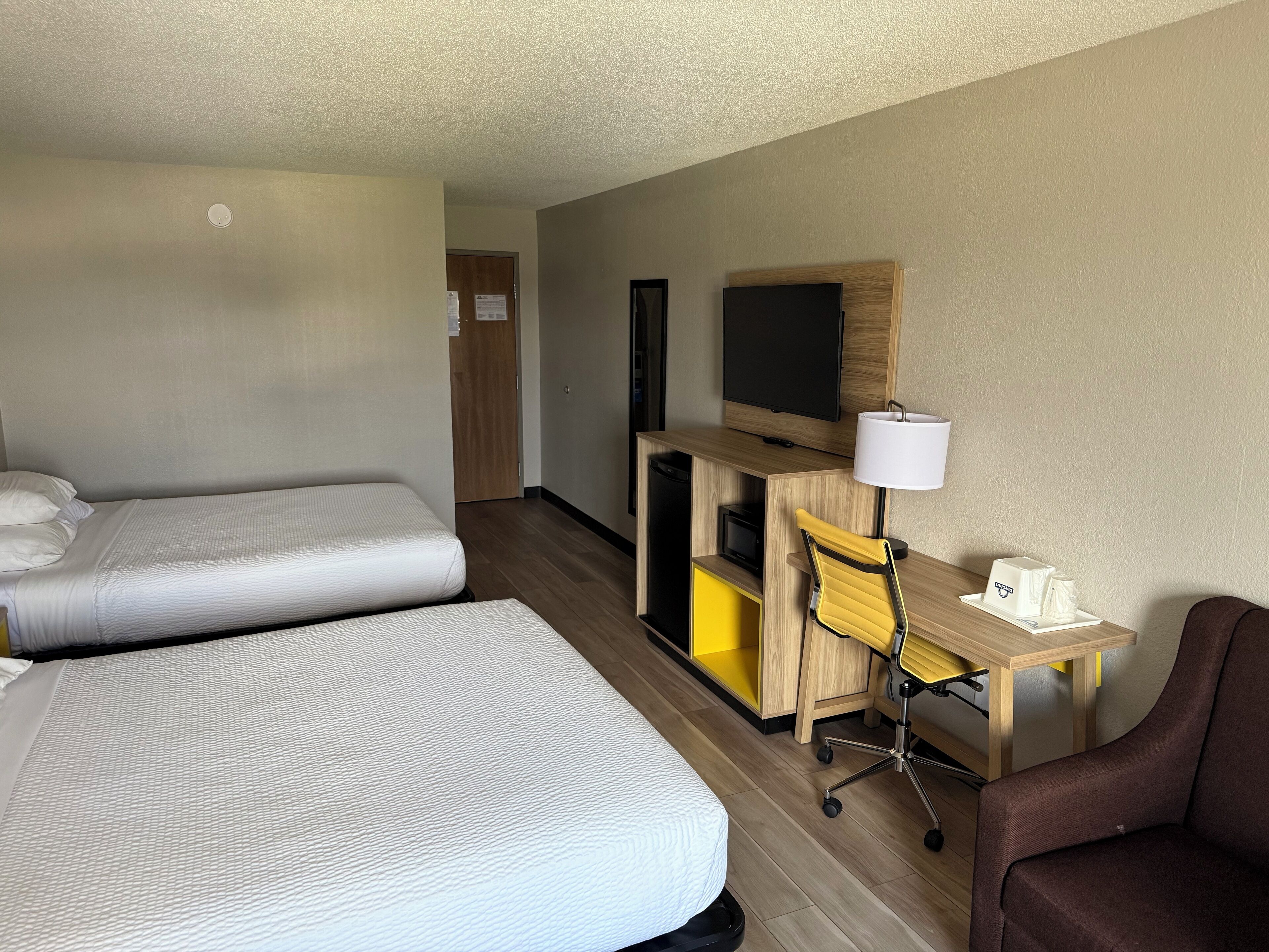 Une chambre d’hôtel avec deux lits, un bureau avec un ordinateur, une chaise, une télévision et une lampe.
