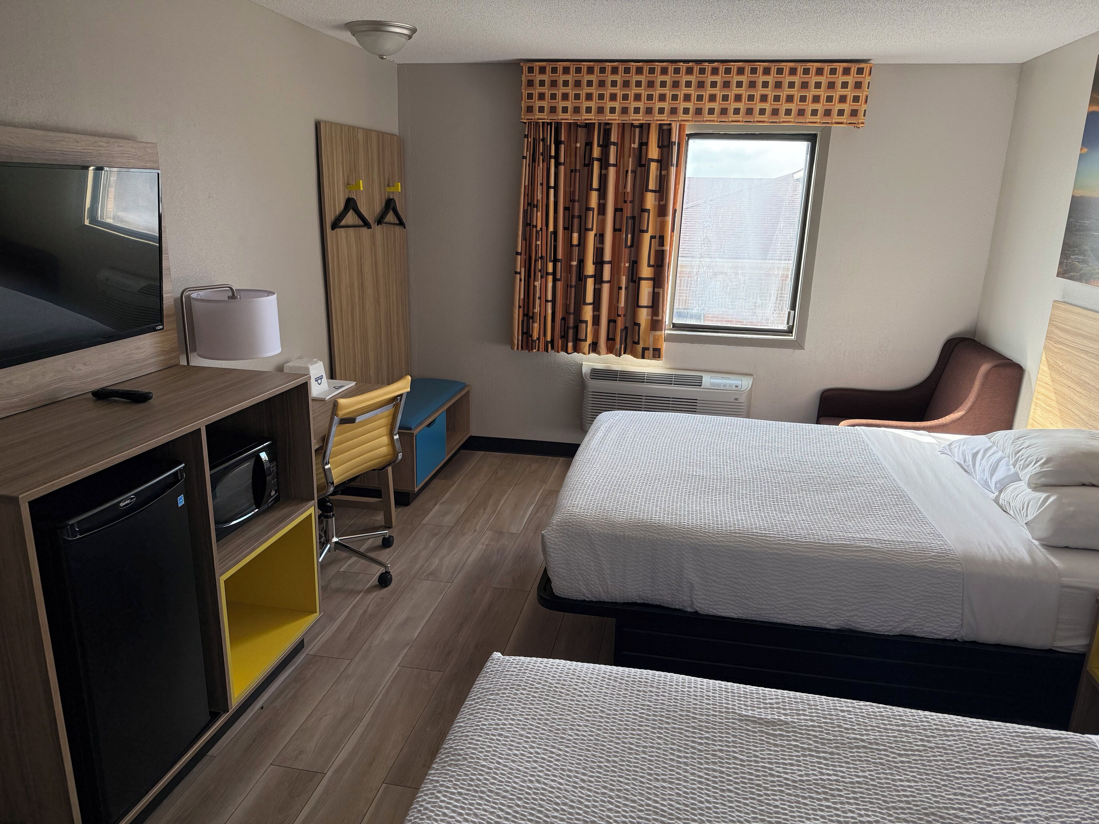 Habitación de hotel con cama, escritorio, televisión, armario y ventana con cortinas.