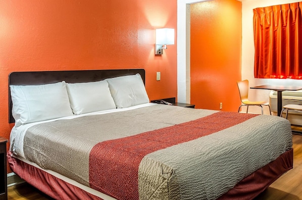 A hotel room with a bed, a nightstand, a table with a chair, and a window with curtains.