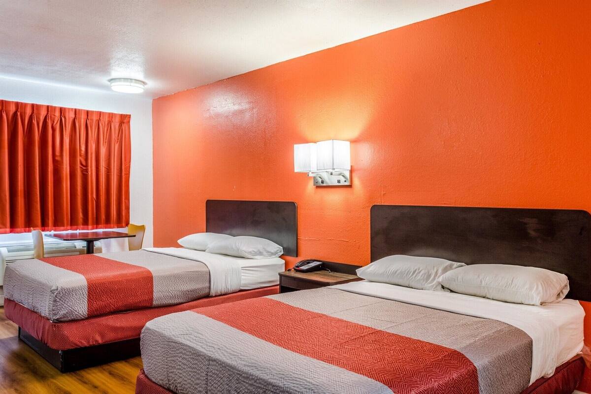 A hotel room with two beds, red curtains, and a wall-mounted light fixture.