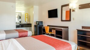 Ein Hotelzimmer mit zwei Betten, einem Schreibtisch, einem Stuhl, einem Fernseher und einem Spiegel.