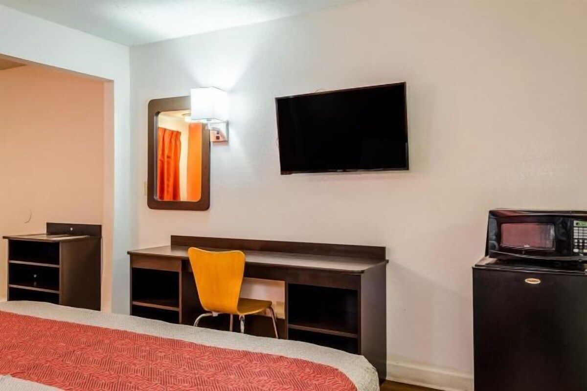 A hotel room with a bed, a desk, a chair, a television, and a microwave.