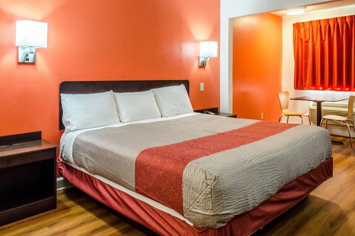 A hotel room with a large bed, two bedside tables, a desk with a chair, and a red curtain.