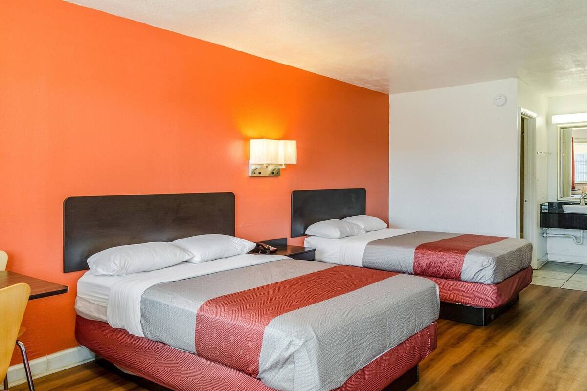 Two beds with headboards, a nightstand, a lamp, and a wooden floor.