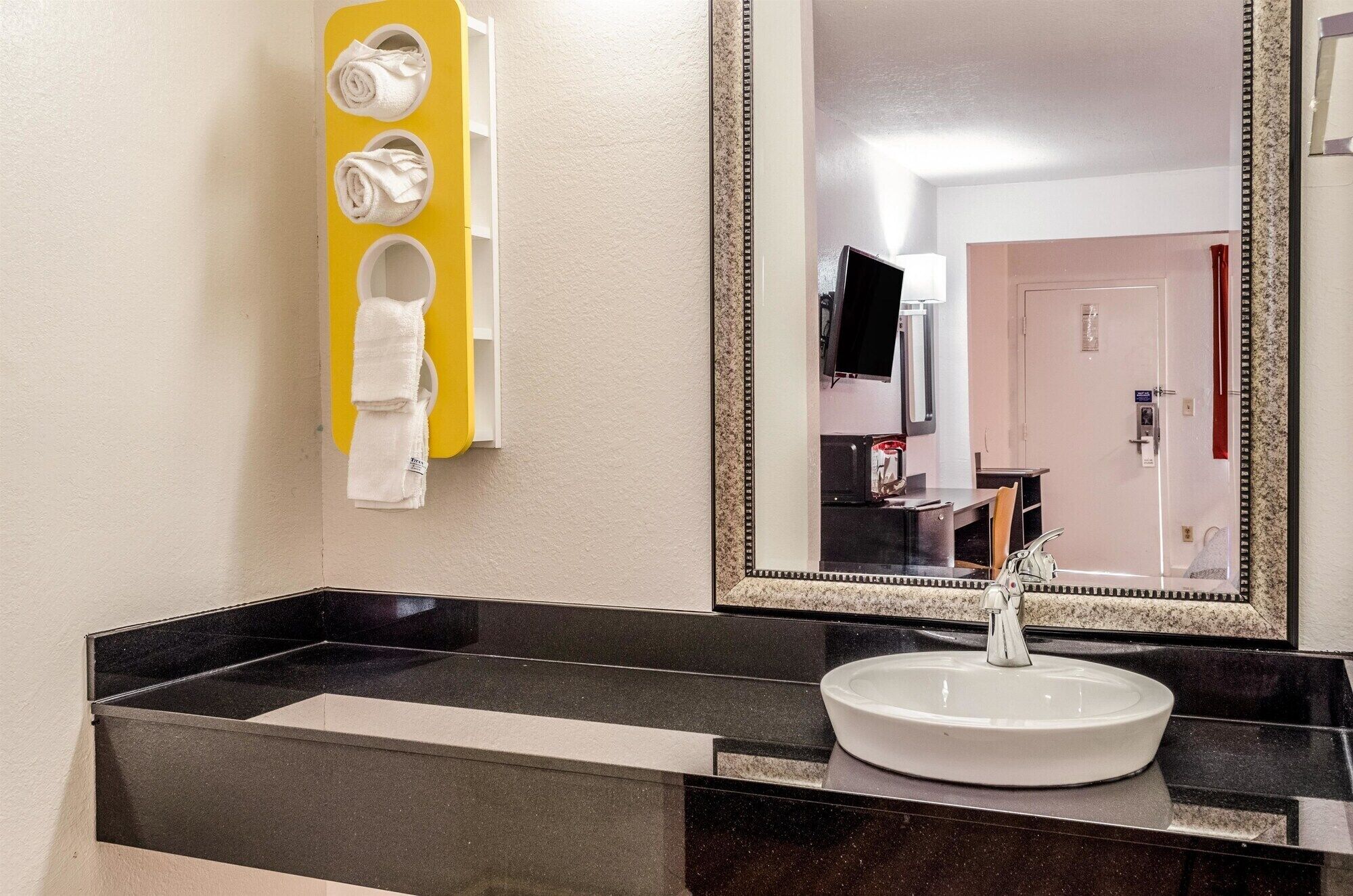 Un baño con lavamanos de mármol negro, un espejo y un dispensador de toallas amarillo.