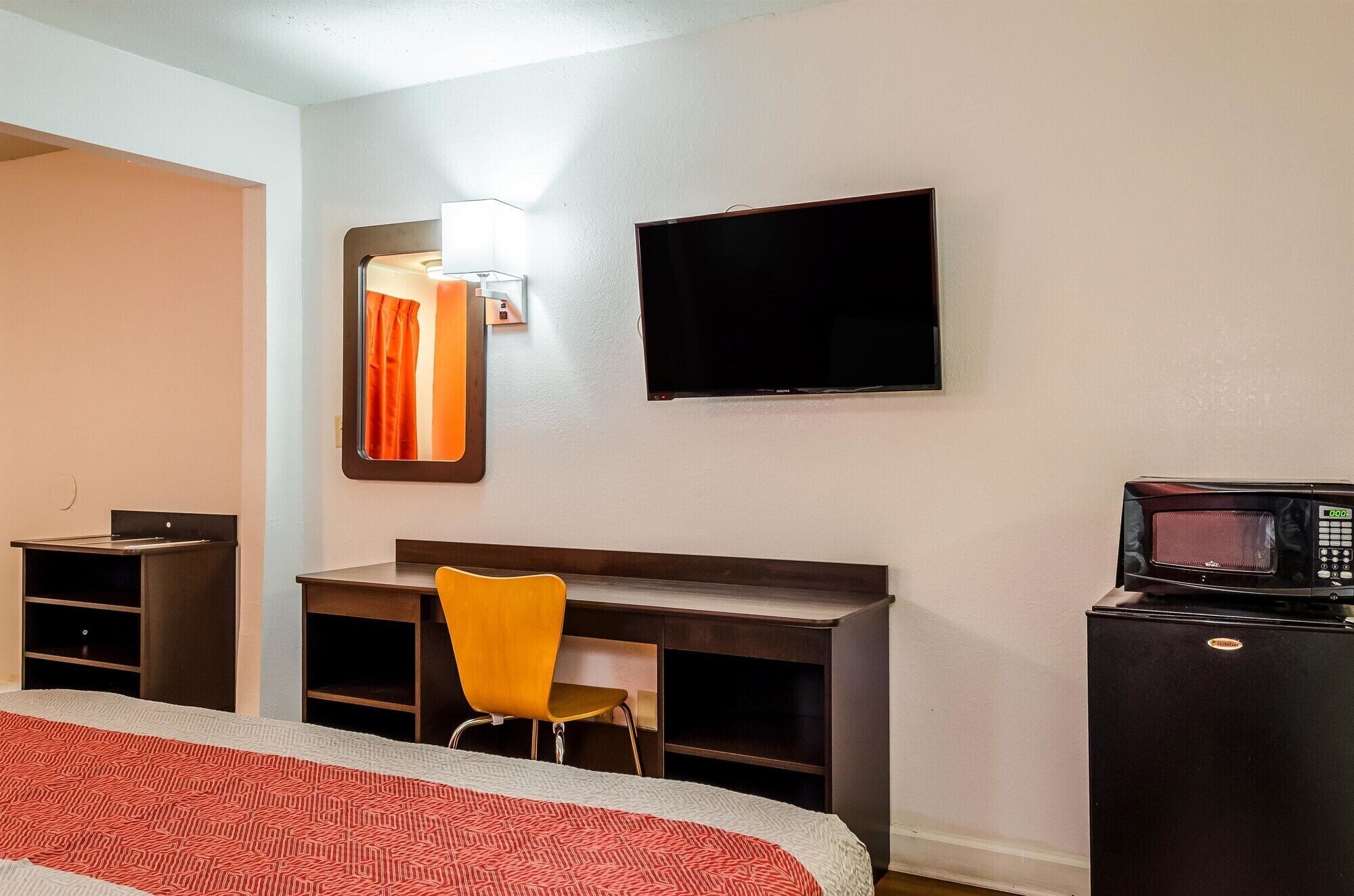 Una camera d'albergo con un letto, una scrivania, una sedia, una televisione e un forno a microonde.