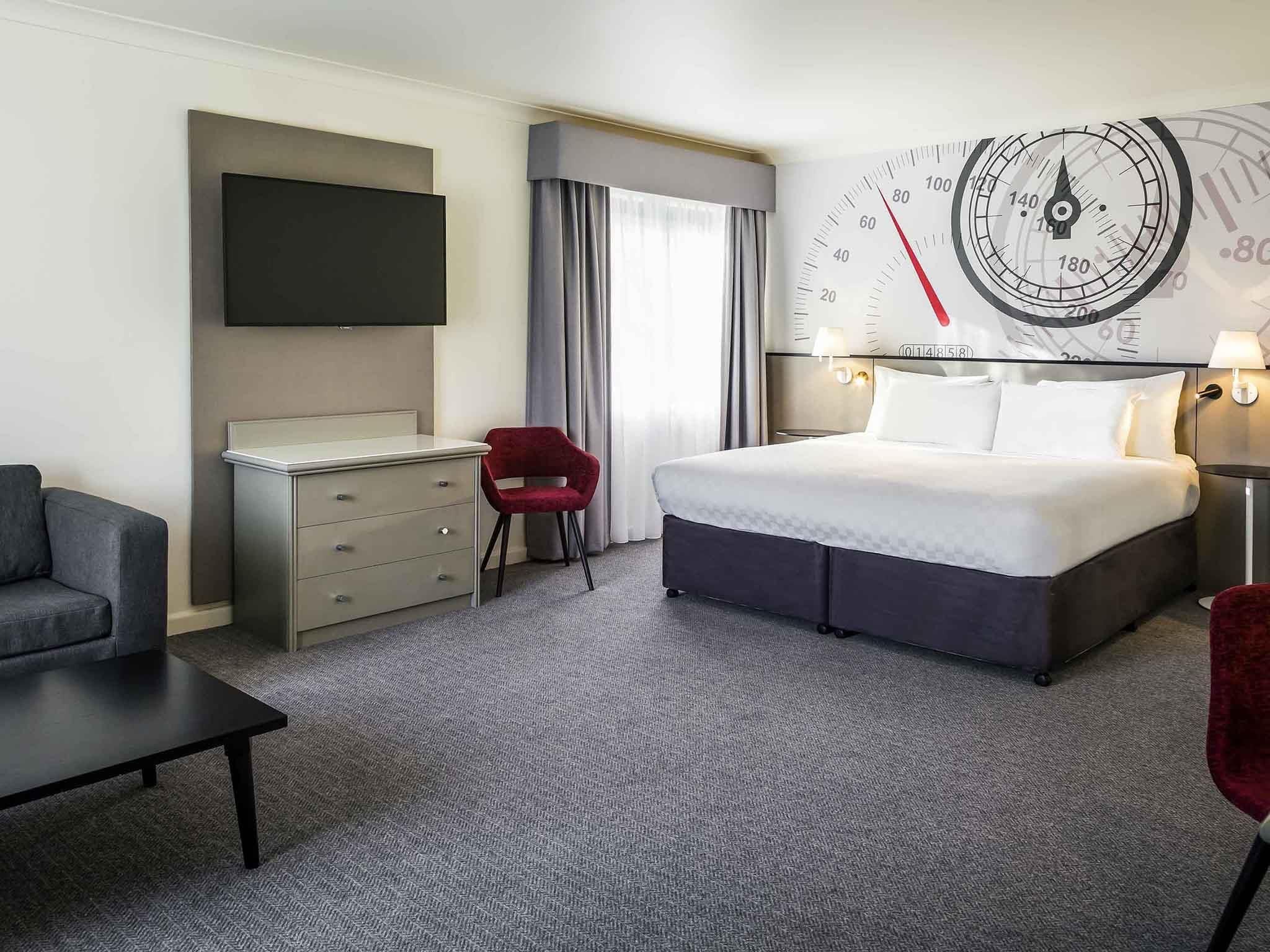 Una camera d'albergo con un letto, una scrivania, una sedia, una televisione e una sveglia a muro.