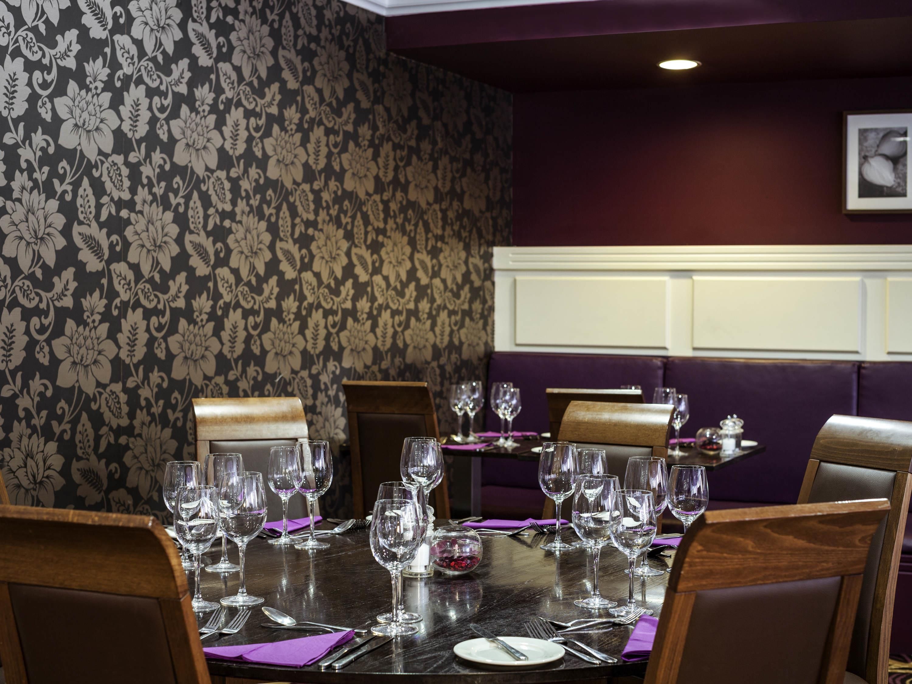 A dining area with a table set for a meal, surrounded by chairs, with a patterned wallpaper and a framed picture on the wall.