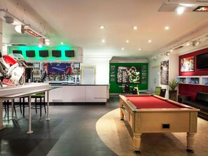 Ein Billardtisch, ein Barbereich mit einer Motorradpräsentation und eine grüne Wand mit Rennsportmemorabilien.