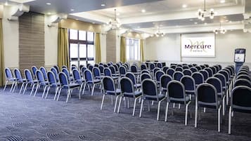 A conference room with rows of chairs, a projector screen, and a Mercure Hotels sign.
