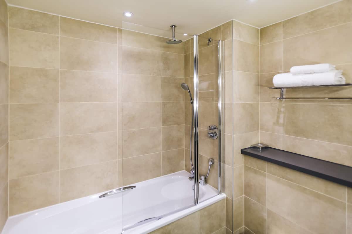 A modern bathroom with a glass-enclosed shower, a white bathtub, and a shelf with towels.