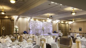 Une salle de banquet avec des tables rondes, des nappes blanches et des chaises ornées de rubans dorés.