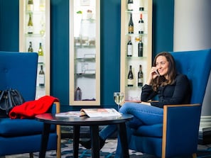 A woman sitting on a blue sofa in a room with a wine display and a table with magazines.