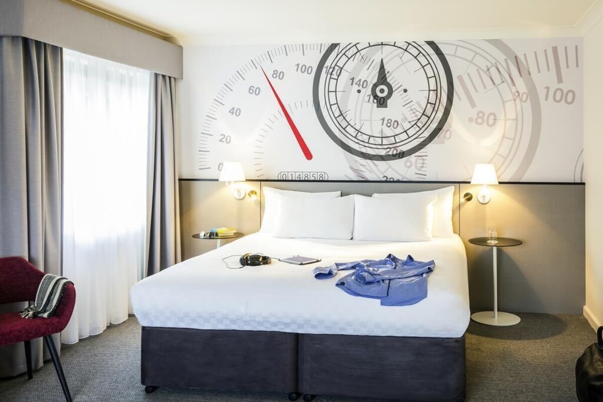 Een hotelkamer met een groot bed, twee bedlampen, een klok aan de muur en een rode stoel.