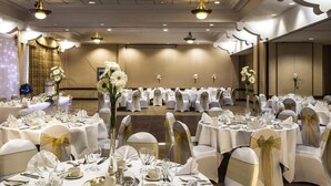 Une salle de banquet avec des tables rondes, des nappes blanches et des chaises ornées de rubans dorés.