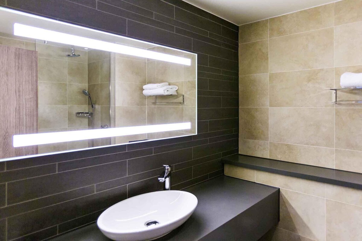 Un baño moderno con un espejo grande, un lavabo y un perchero para toallas.