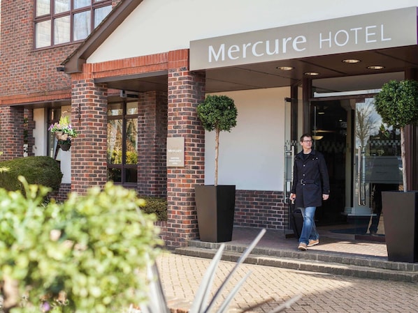 The entrance to Mercure Hotel with a brick facade, a signboard, and a welcoming sign.