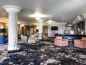 A hotel lobby with a reception desk, seating areas, and a bar.