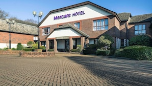 A Mercure Hotel with a brick facade, a clear blue sky, and a paved entrance area.