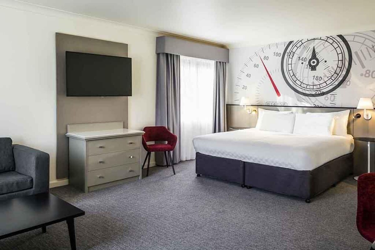 Een hotelkamer met een bed, een bureau, een televisie, een klok en een rode stoel.