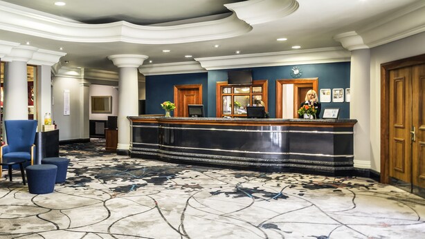 Un hall d’hôtel avec un sol en marbre, un comptoir d’accueil et une chaise bleue.
