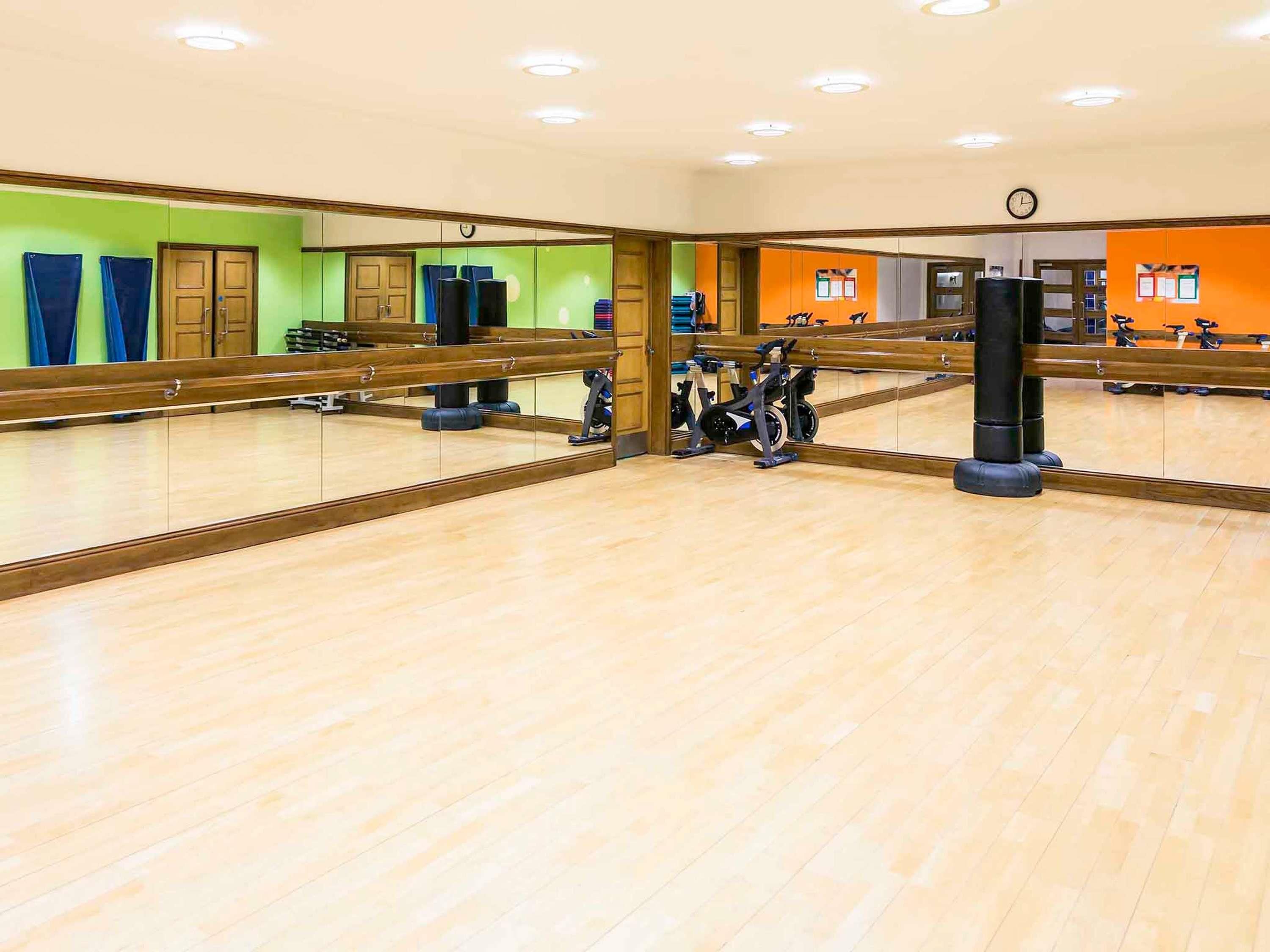 A gym with exercise equipment, a large mirror, and wooden flooring.