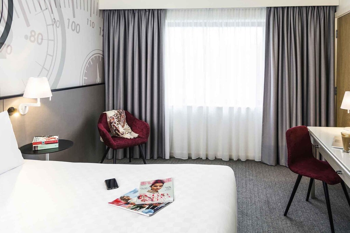 Una habitación de hotel con una cama grande, dos sillas, un escritorio y un reloj en la pared.