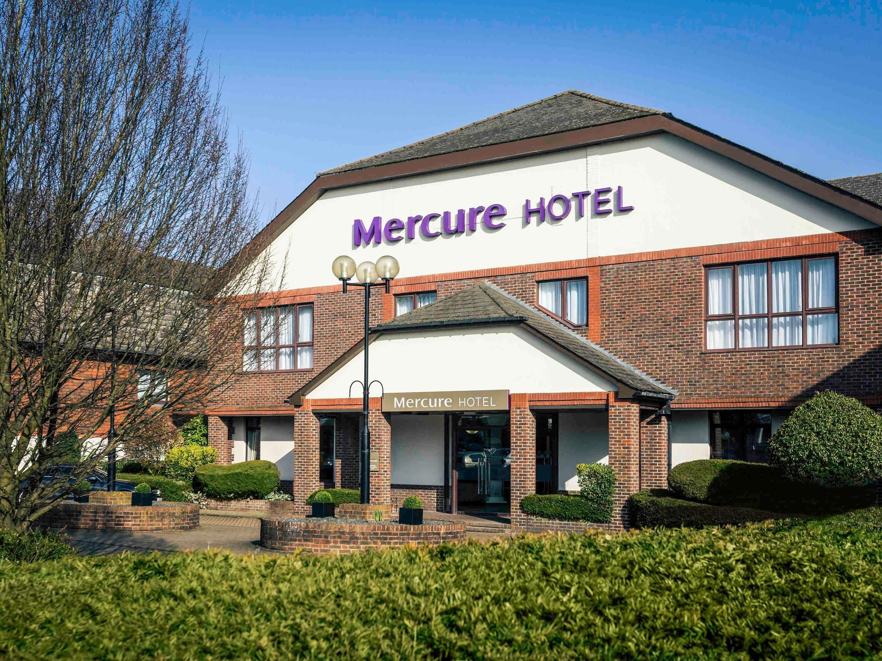 A Mercure Hotel with a brick facade, a prominent sign, and a well-maintained front garden.