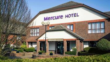 A Mercure Hotel with a brick facade, a prominent sign, and a well-maintained front garden.