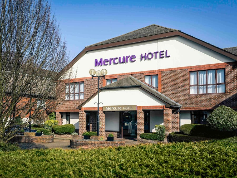 A Mercure Hotel with a brick facade, a prominent sign, and a well-maintained front garden.
