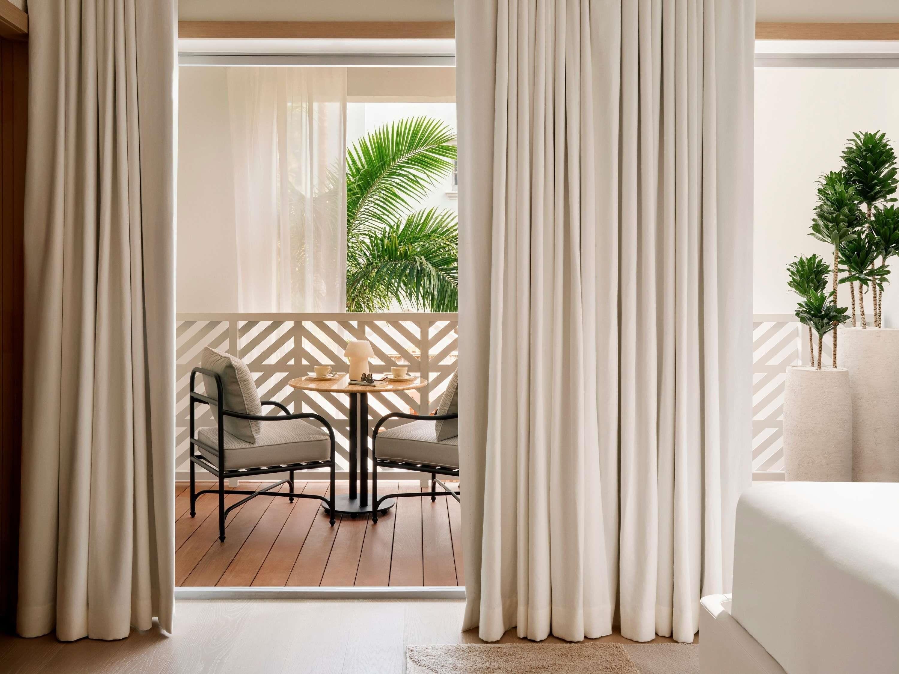 A room with a view of a balcony, a round table with chairs, and a bed.