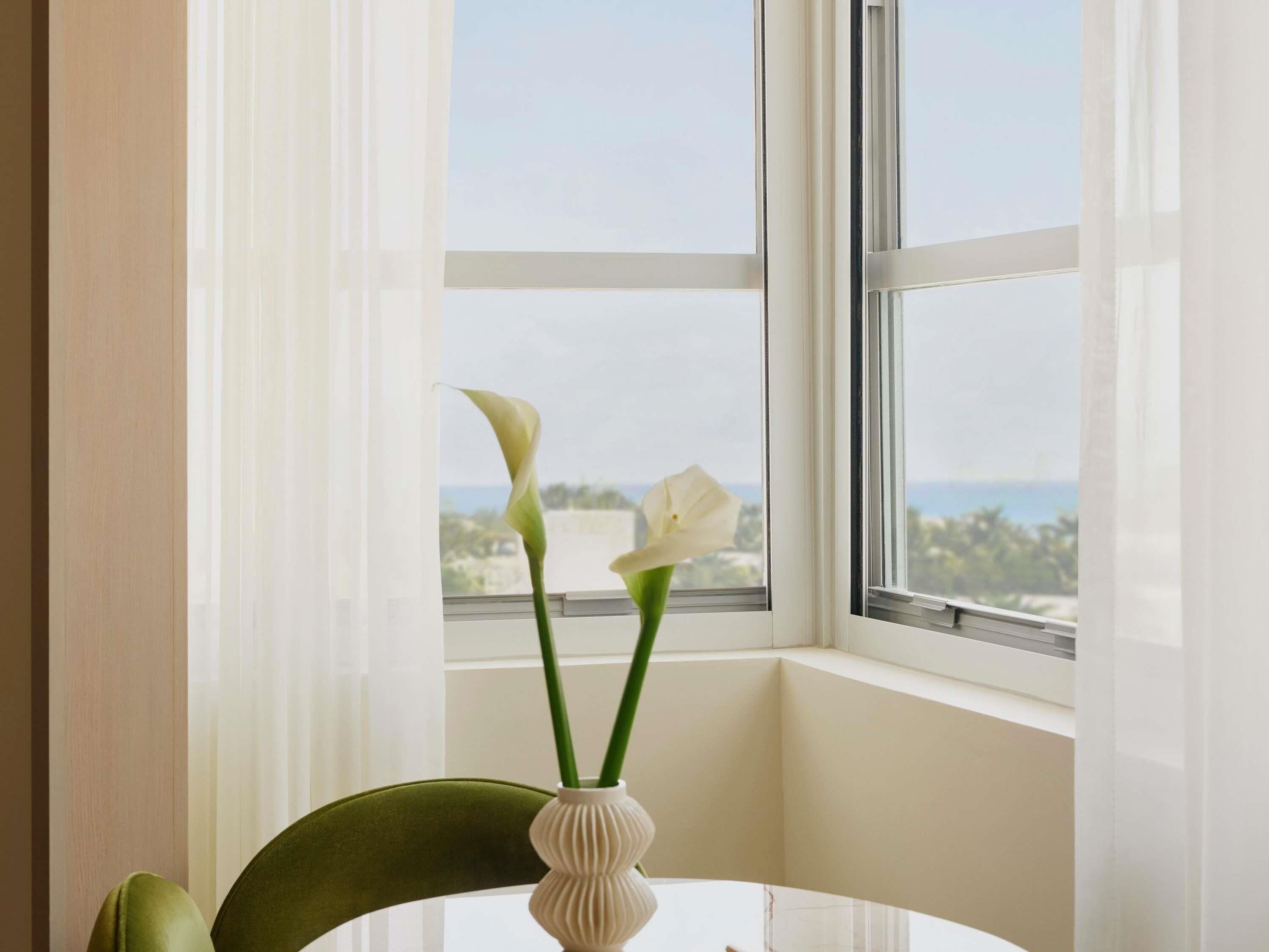 Ein Tisch mit Blumen in einer Vase und ein grüner Stuhl in einem Zimmer mit einem Fenster.