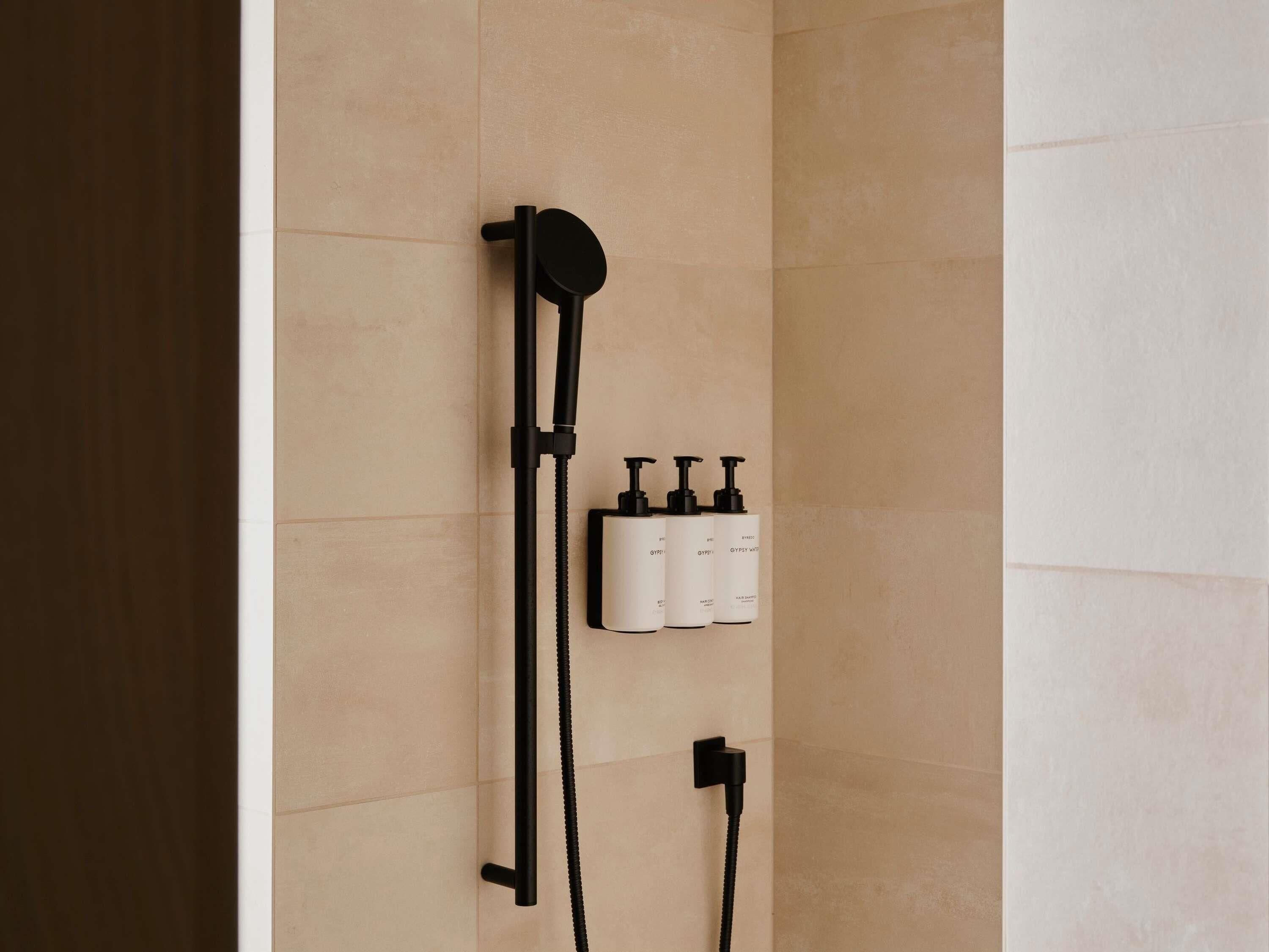 A shower with a handheld showerhead, a handheld shower attachment, and a wall-mounted control panel with three bottles.