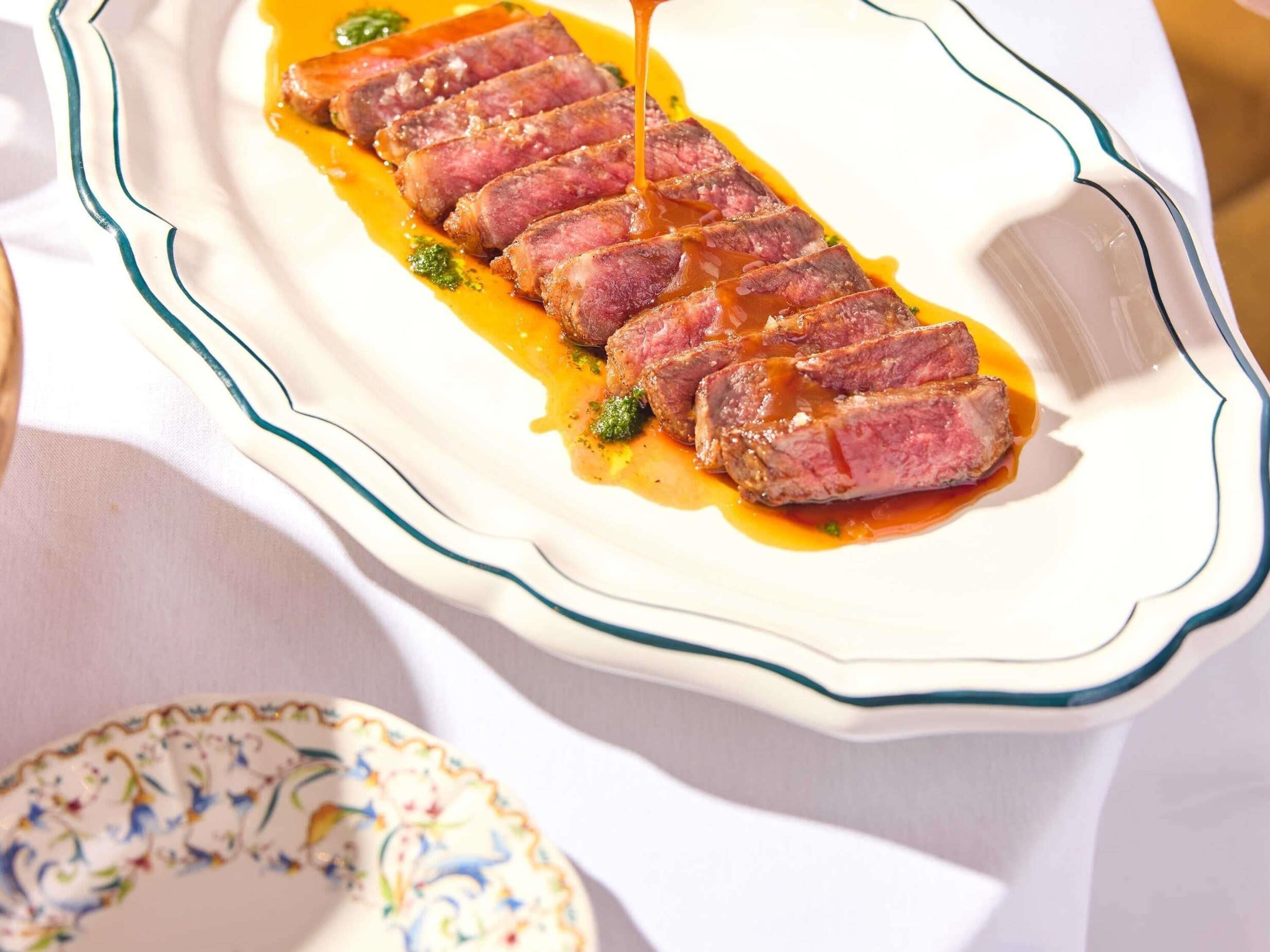 A white plate with a blue rim containing sliced meat and a sauce, placed on a table.
