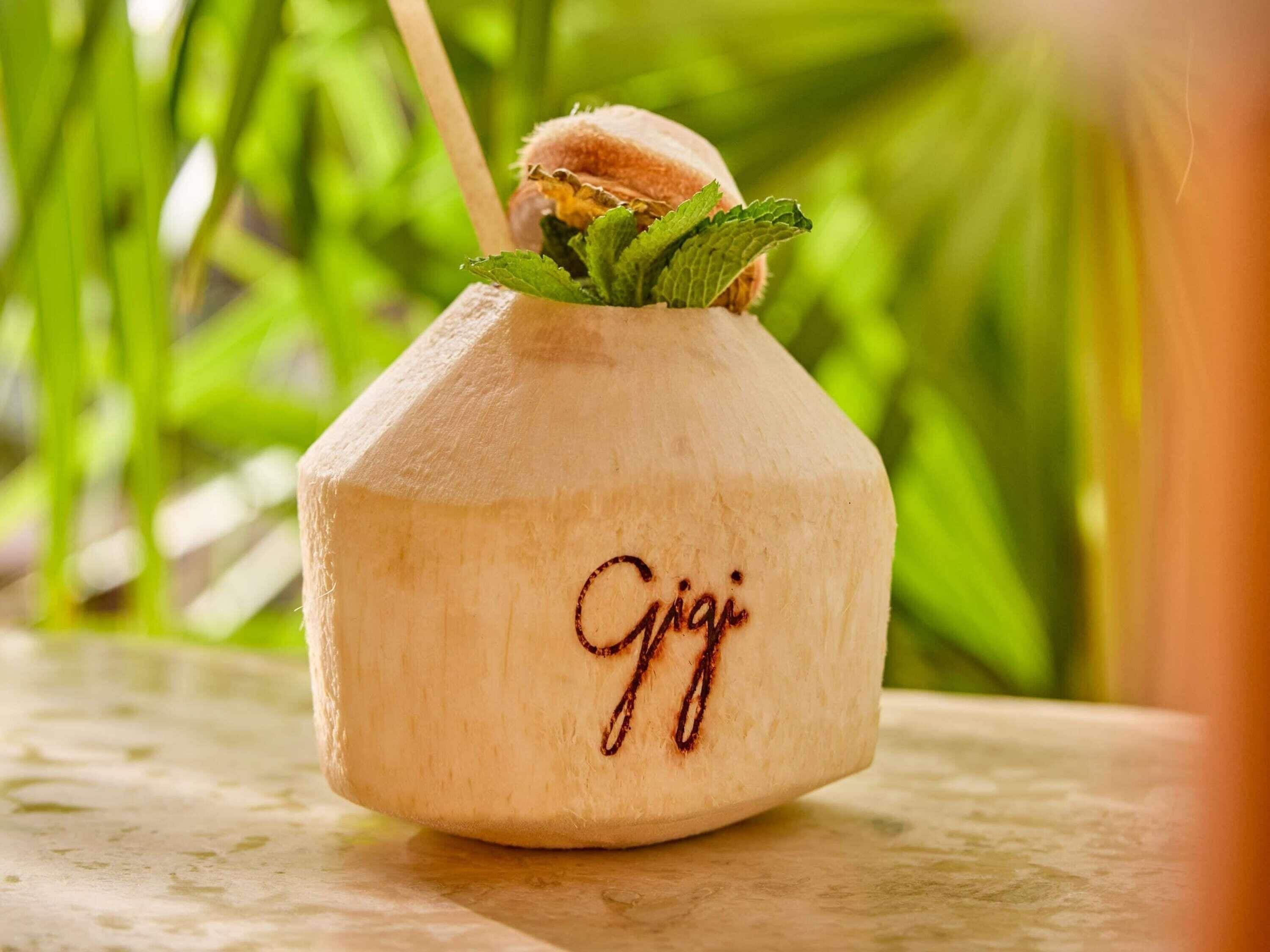 A coconut drink with a straw and mint leaves, labeled 'Gijai' on a wooden surface.