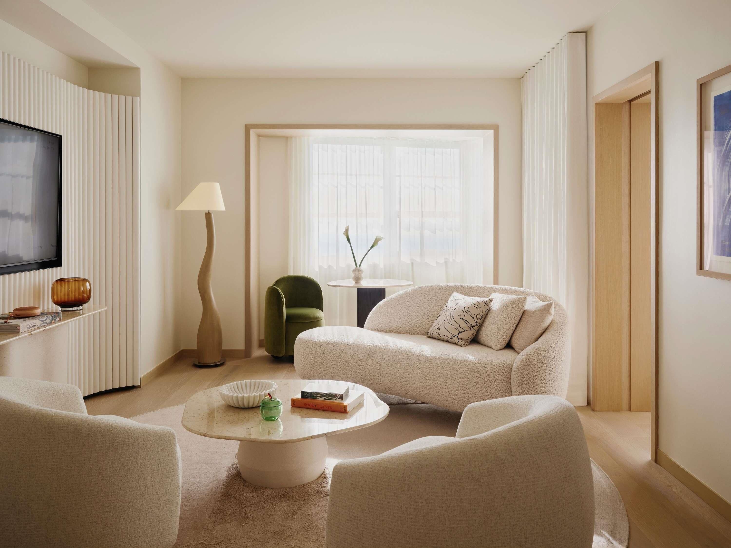 Una sala de estar moderna con un sofá, sillones, una mesa de centro, un televisor y un ventanal con cortinas.