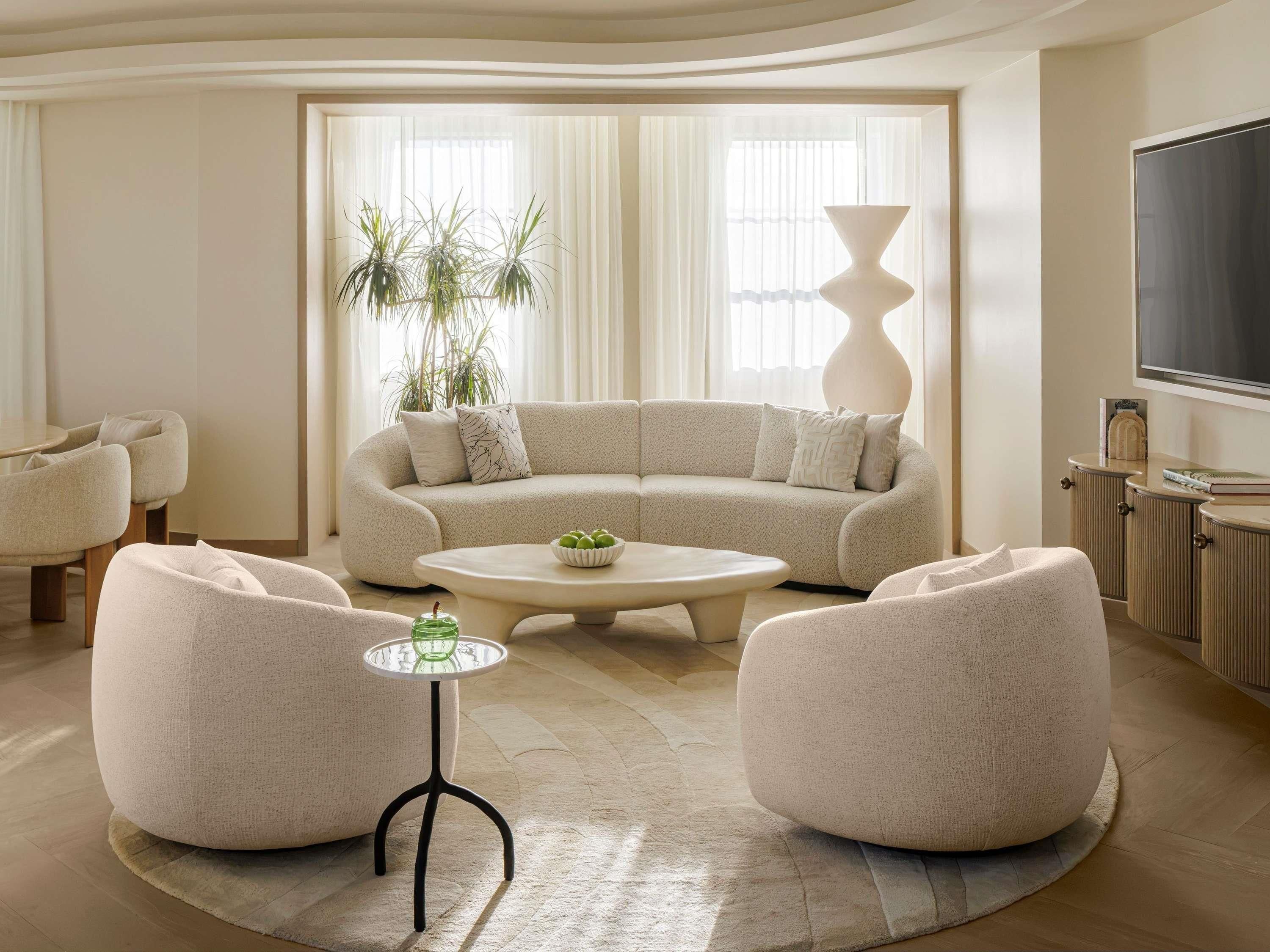 Una sala de estar moderna con un sofá curvo, dos sillones, una mesa de centro y un televisor.
